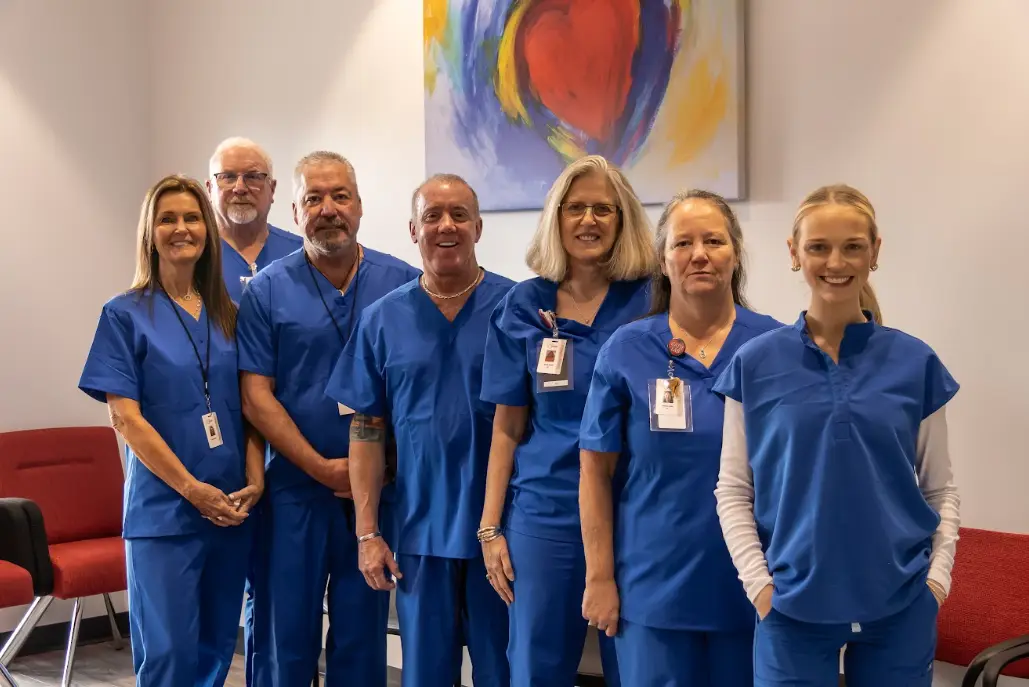 Jeffrey G. Tauth, M.D., F.A.C.C., with his staff in blue scrubs, standing in front of a painting of a heart
